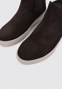 Bottines en daim marron avec une finition texturée, bout rond et semelle en caoutchouc clair. Elles disposent de panneaux élastiques sur les côtés pour un enfilage facile.