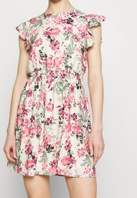 Kukkamekko, jossa on lyhyet röyhelöpaidat, kapealla vyötäröllä ja vaalean kermansävyisellä pohjalla pinkki- ja vihersävyisiä kukkakuoseja.