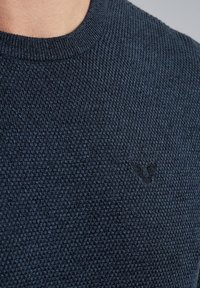 Dunkelblau gestrickter Pullover mit einem strukturierten Muster. Verfügt über ein geripptes Halsbündchen und ein dezentes schwarzes Logomotiv auf der Brust.