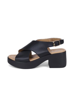 Sandale en cuir noir avec larges brides croisées, semelle intérieure rembourrée couleur cuir clair, talon bloc épais et bride de cheville réglable avec boucle.