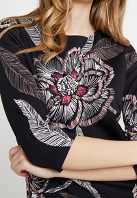 T-shirt noir avec des broderies florales complexes en rose et blanc, manches trois-quarts, col rond et texture douce.