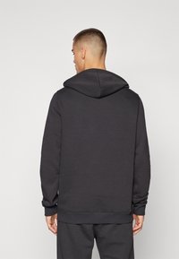 Haut à capuche gris foncé avec une coupe décontractée, doté d'une capuche à cordon et de poignets côtelés. Fabriqué en tissu doux et texturé avec un design sobre au dos.