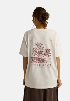 Biała, bawełniana koszulka oversize z czerwoną grafiką przedstawiającą palmy i lamparczycę oraz napisem „JUNGLE SPIRIT” na plecach.