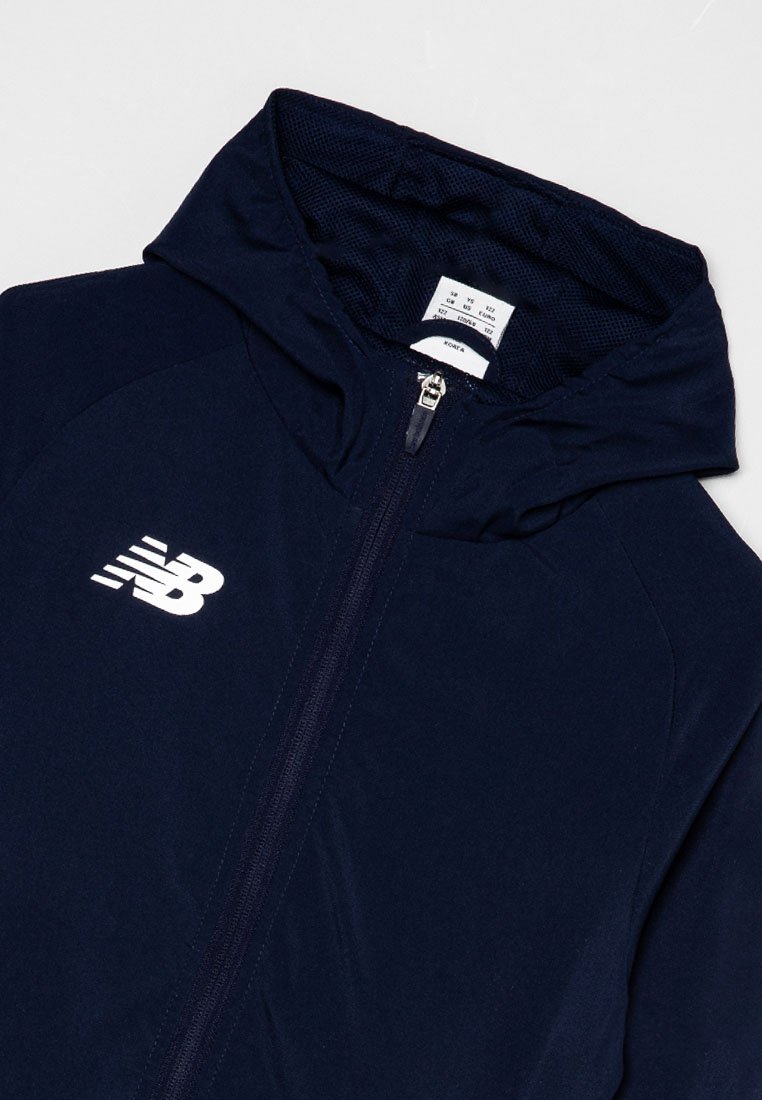 Marineblauwe ritsjack met capuchon, voorzien van een wit New Balance-logo, een gladde textuur en een binnenvoering van gaas. Inclusief label met maatinformatie.