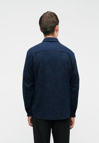 Marineblauwe button-up shirt gemaakt van textuurstof, met een kraag, lange mouwen en een gebogen zoom. Zichtbaar knoopdetail op de mouw.
