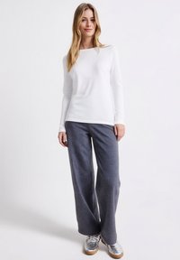 Hvid langærmet top kombineret med grå, stribede bukser med vide ben, med en glat tekstur og subtile linjer, fuldendt med metalliske sneakers.