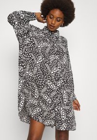 Vestido de mangas compridas em preto e branco com padrão abstracto, colarinho alto e corte descontraído. Tecido suave e detalhes de fenda lateral.