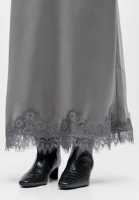 Jupe en satin gris avec un détail d'ourlet en dentelle complexe à motif floral ; associée à des bottines en cuir noir embossé effet crocodile.