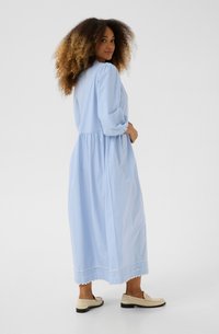 Light blue cotton dress with puff sleeves, gathered waist, and scalloped hem detail. Paired with cream loafers.