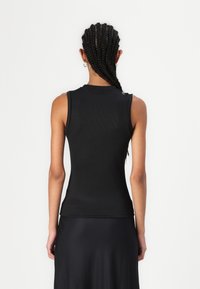 Zwarte geribbelde tanktop met hoge halslijn, mouwloos ontwerp en aansluitende snit, gecombineerd met een vloeiende zwarte rok.