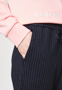 Ljusrosa sweatshirt med "ARMANI"-logotyp, i kombination med marinblå randiga byxor som har en ficka och dragsko i midjan. Texturerad tyg.