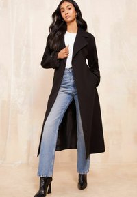 Melnā garā mētelī ar apkakli, apvienots ar gaiši ziliem taisnajiem džinsiem un melniem augstpapēžu zābakiem. Gluda materiāla un atvērta priekšpuse.