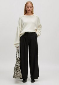 Overmaat crèmekleurige sweater, zwarte wijde broek en zwarte schoenen. Gecombineerd met een gestreepte zebra-print tas met trekkoord. Minimalistische stijl.