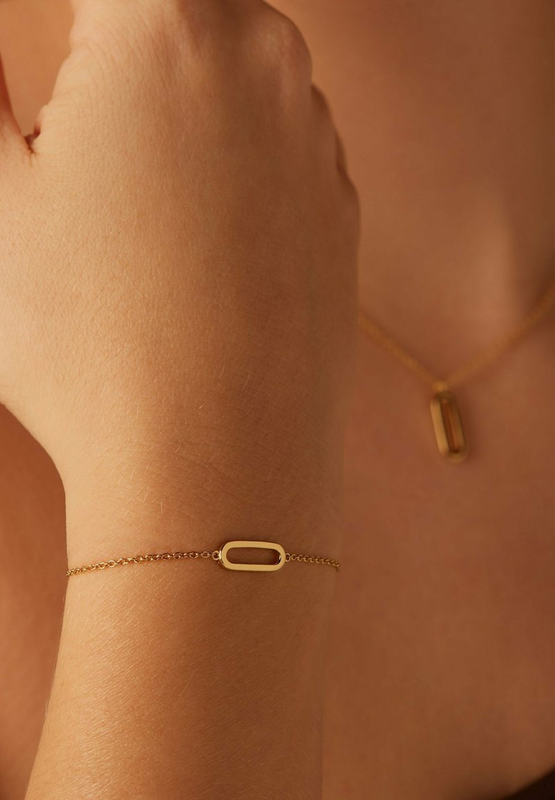 Bracelet en chaîne dorée avec un charm ovale. Texture lisse, maillons délicats. Assortie à un collier similaire, également avec un pendentif ovale.