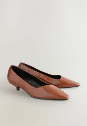 Bruna läderpumps med spetsig tå och låg klack, med en slät yta och minimalistisk design. Svart inredning.