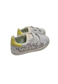Sneaker bianco con un accento giallo, progettato con due strap in Velcro, caratterizzato da motivi floreali e a stelle sui lati. Suola in gomma.