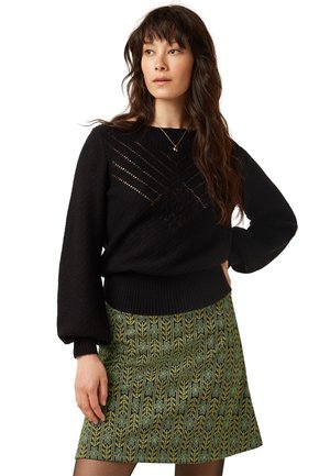 Pull en maille noir avec motif texturé et ourlet côtelé, associé à une jupe verte à motif floral et de feuilles.
