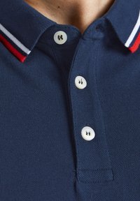 Marineblauwe poloshirt van een textuurstof, met een klassieke kraag, drie witte knopen en rood-witte strepen op de kraag.