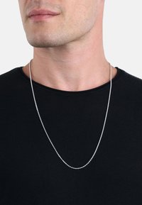 Silverkedja hängande över en svart t-shirt. Designen har ett fint mönster med runda länkar och en slät, polerad yta.