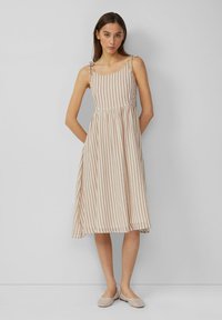 Gestreiftes Kleid in hellem Beige und zartem Rosa, mit verstellbaren Trägern, einem taillierten Oberteil und einem ausgestellten Rock, kombiniert mit flachen Schuhen.