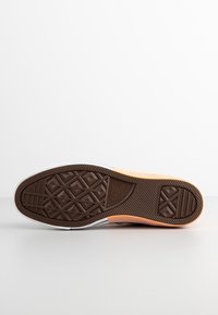 Semelle en caoutchouc marron d'une basket Converse All Star avec un motif de semelle géométrique sur une surface et un fond blancs.