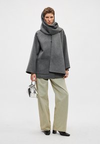 Hall hall villastest mantlig laia varrukate ja nööpidega, mida on kombineeritud ülisuurte kahvaturoheliste pükste ja väikese hõbedase kotiga.