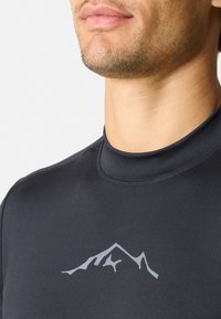 Zwarte, vochtafvoerende rash guard met een hoge hals. Heeft een lichtgrijs berglogo op de borst. Glad, elastisch textuur.