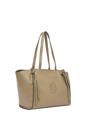 Béžová kožená taška přes rameno s dvojitými ramenními popruhy, dekorativními třásněmi na bocích a vyšitým emblémem na přední straně, na bílém pozadí.