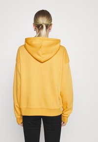 Sweat à capuche jaune avec une coupe décontractée, épaules tombantes et ourlet côtelé. Texture lisse et design simple, sans motifs ni accents visibles.