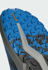 Terränglöpningsskor med en blå gummiyttersula som har vinklade klackar, grå detaljer och "Continental"-logotypen.