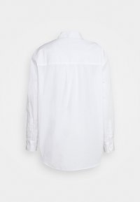 Camicia bianca a maniche lunghe con colletto e polsini a bottoni, caratterizzata da una linea dritta e una texture liscia, senza motivi o accenti visibili.