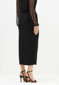 Czarna spódnica o dopasowanym kroju, do kolan. Przezroczyste, długie rękawy w kropki. Dopasowana z czarnymi sandałami na wysokim obcasie z paskami. Gładka tekstura.