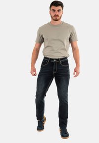 Pantalones vaqueros de mezclilla azul oscuro con un corte recto, que presentan costuras en contraste y un diseño clásico de bolsillo frontal. Combinados con una camiseta gris claro.