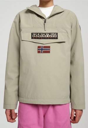 Beiger Pullover mit frontaler Klappentasche, Napapijri Geographic Logo, norwegischem Flaggenaufnäher, kombiniert mit knallpinken Hosen.