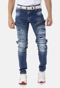 Dunkelblaue Jeans aus Denim mit Ripped-Details und tailliertem Schnitt. Mit einem weißen, mit Nieten besetzten Gürtel und gesteppten Akzenten.