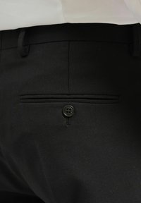 Svarta skräddarsydda byxor med en dubbel kantficka med knappstängning och subtilt strukturtyg.