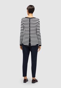 Cardigan à rayures noires et blanches avec manches longues, doté d'une fermeture boutonnée au dos et d'un col arrondi. Associé à un pantalon bleu marine et des chaussures assorties.