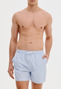 Niebieskie i białe kąpielówki w paski z elastycznym pasem, sznurkiem i bocznymi kieszeniami. Materiał ma gładką teksturę.
