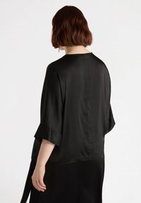Black, smooth, long-sleeve top with a relaxed fit; features a subtle sheen, rounded hem, and loose sleeves with a slight cuff.