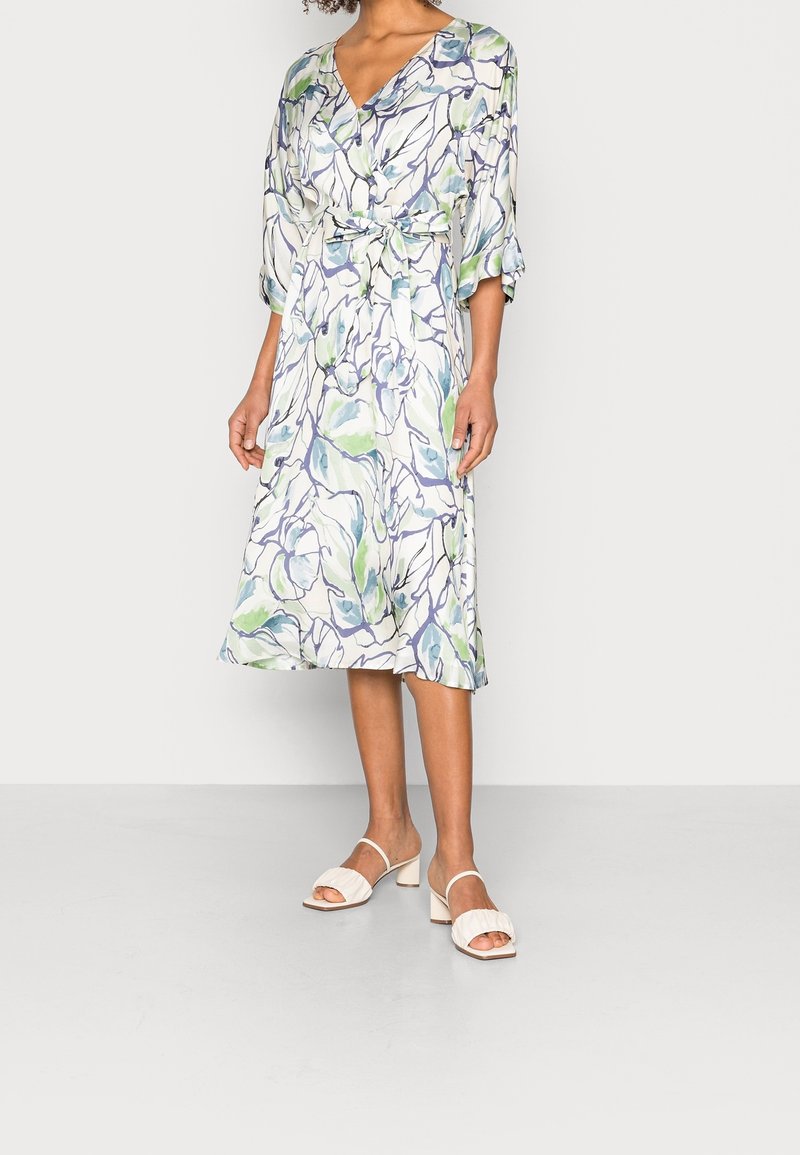 Robe midi à imprimé floral en tissu léger, dotée d'une ceinture à la taille, d'un col en V et de manches trois-quarts. Sandales blanches à talons avec des brides côtelées.