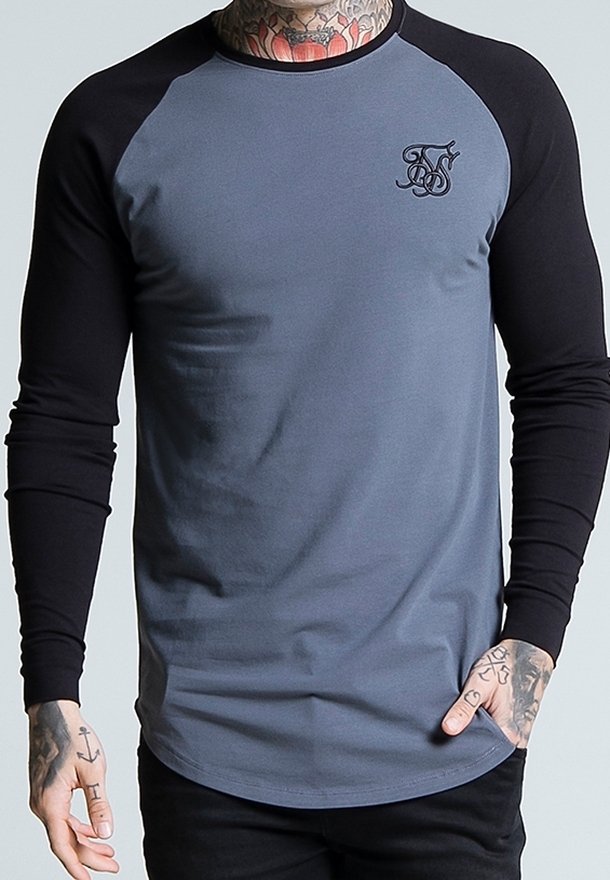 T-shirt raglan à manches longues gris et noir avec un ourlet arrondi, arborant un petit logo sur la poitrine et une texture de coton lisse.