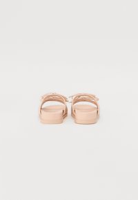 Lys rosa flate sandaler med tynne, kryssende stropper og en glatt matte finish. Enkelt design med rund tå og polstret såle.