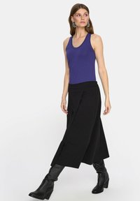 Fioletowy top na ramiączkach, szerokie czarne culotte i czarne botki do kolan. Ubranie ma luźny krój i warstwowe tekstury.