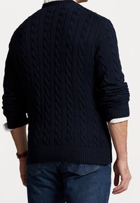 Mörkblå kabelstickad tröja med ribbstickade muddar och fåll, med en synlig vit skjortkrage under. Avslappnad design, texturerat tyg.