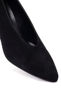Escarpin noir en cuir suede à talons hauts avec un bout pointu et un design subtil de découpes. Doublure intérieure lisse et silhouette élancée.