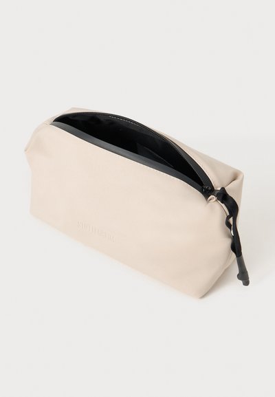 Neceser de silicona beige con cierre de cremallera y un interior negro. Presenta una superficie texturizada y una pequeña lengüeta negra en la cremallera.