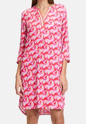 Femme portant une robe à motifs rose et rouge jusqu'aux genoux, manches trois-quarts et encolure en V avec bordure rayée.