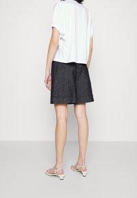 Witte blouse met korte mouwen en opgerolde mouwen, gecombineerd met donkere denim shorts met een omgeslagen zoom en twee achterzakken, gedragen met witte hoge sandaaltjes.