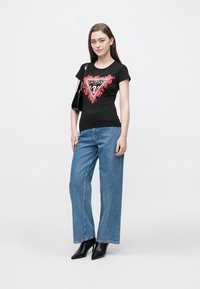 Black cotton T-shirt with a red floral triangle graphic and "GUESS" text; paired with light blue wide-leg jeans and black heeled ankle boots.