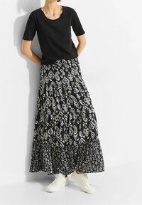 Haut noir à manches courtes associé à une jupe maxi à volants noire et blanche imprimée de motifs floraux et cachemire. Stylé avec des baskets blanches.